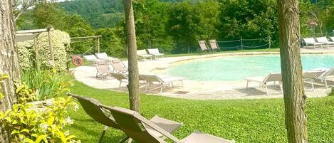 Zona de piscina con sillones de descanso, un pérgola y vistas a la montaña.
