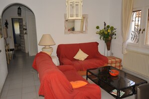 A living room with a red sofa, a glass coffee table, a lamp, a mirror, and a window with curtains. - Villa 6-8 person private property private pool 800 meters from the sea (Miami Platja)