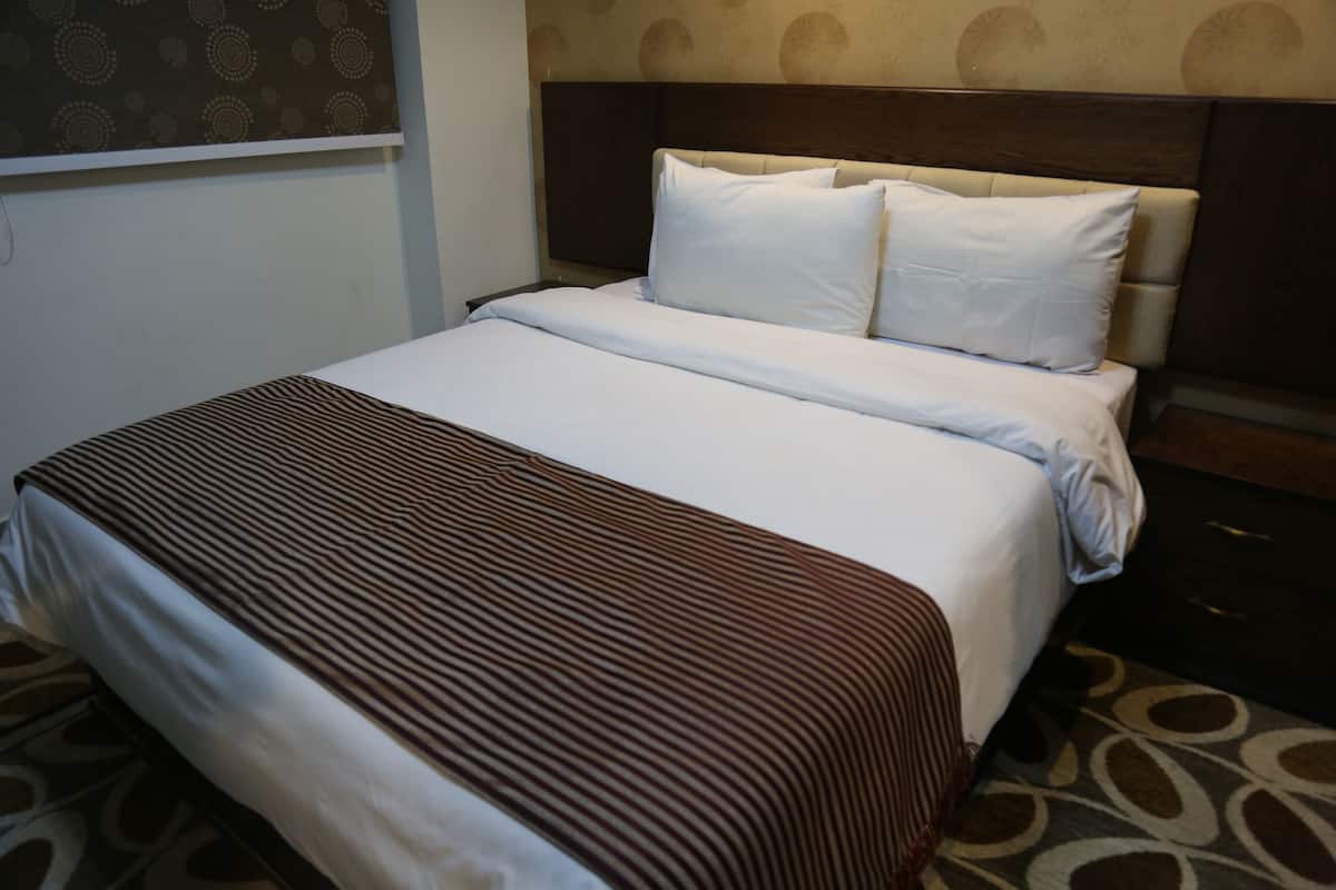 A neatly made bed with a striped bedspread and two pillows, a headboard with a dark wood finish, and a patterned carpet.