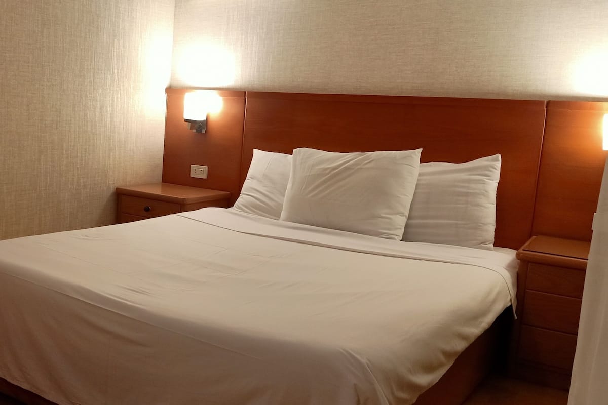 A hotel room with a large bed, a wooden headboard, and a nightstand with a lamp.