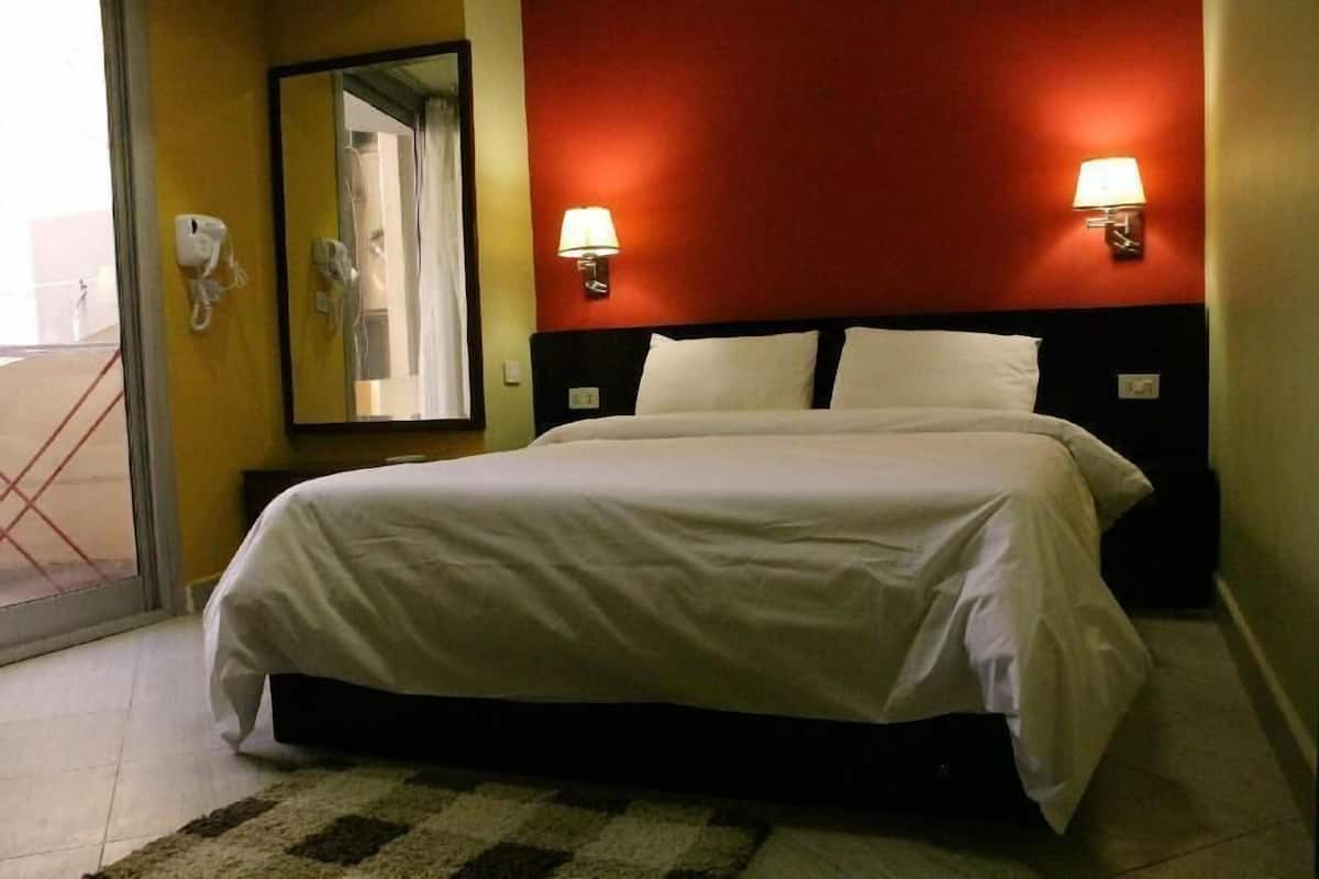 A hotel room with a bed, two bedside lamps, a mirror, and a telephone on the wall.