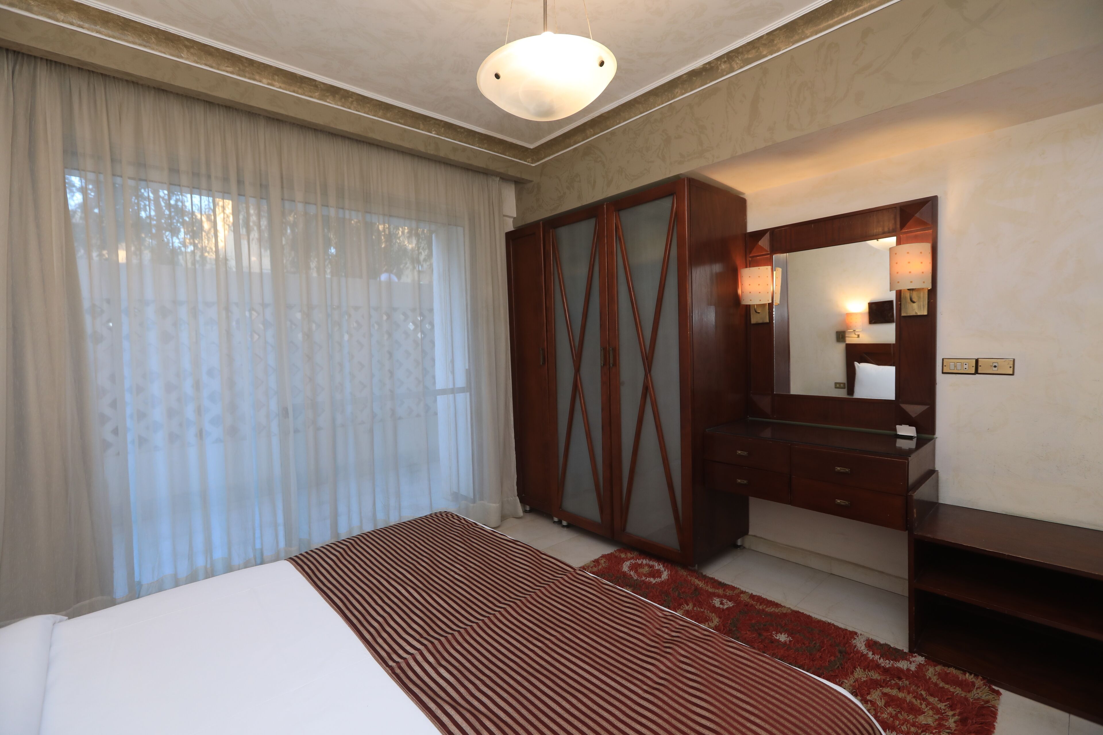 Une chambre à coucher avec un grand lit, une armoire, un miroir et un luminaire au plafond.