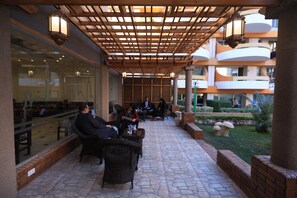 Un espace extérieur aménagé avec des meubles en osier, une pergola ornée de lanternes suspendues et une vue sur l’intérieur du bâtiment.