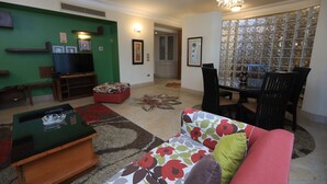 Un salon avec un mur vert, un téléviseur, une table basse, un canapé et un coin repas avec des chaises.