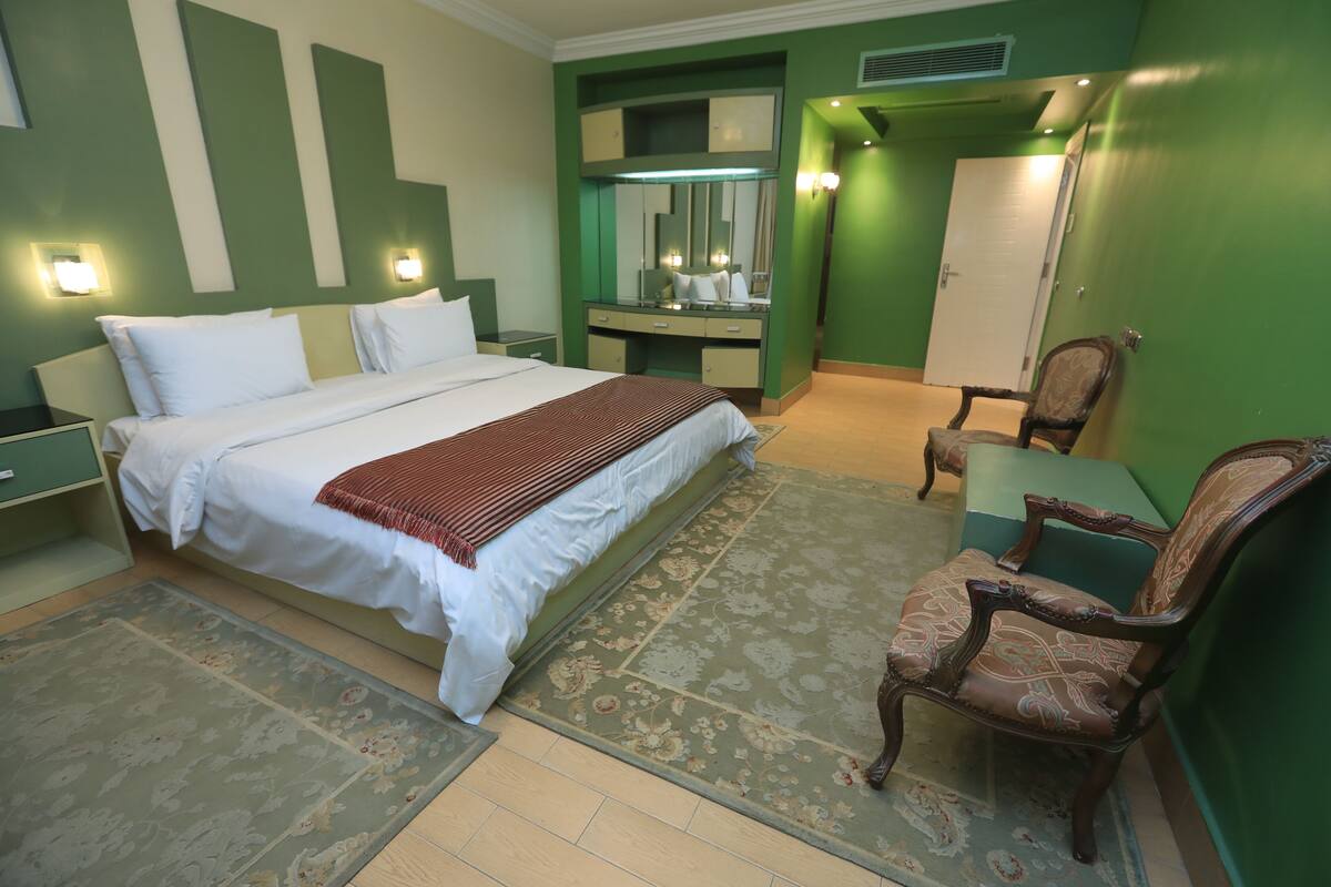 A hotel room with a bed, a dresser, a mirror, a chair, and a door.