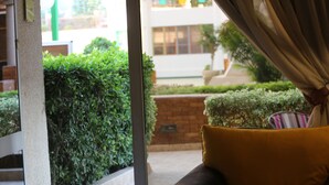Une vue depuis une fenêtre, avec un coussin jaune, une haie verte et un mur de briques.