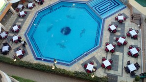 Une piscine octogonale dotée d’un élément circulaire central, entourée d’espaces de détente en plein air avec des tables et des chaises.
