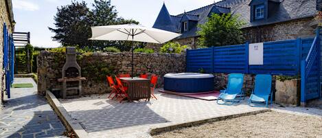 A stone-walled outdoor patio with a table and chairs, a hot tub, and blue chairs.