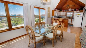A dining area with a glass table and wicker chairs, a kitchen with wooden cabinets and a refrigerator, and large windows with curtains. - Oceanside, Close to beach, Private Pool, Hot Tub, GF1, Ternabout (Duck)