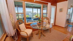 A cozy room with a glass table, wicker chairs, and a view of houses through large windows. - Oceanside, Close to beach, Private Pool, Hot Tub, GF1, Ternabout (Duck)