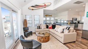 A spacious living area with a large window, a glass coffee table, a beige sofa, and a dining area with a kitchen in the background. - Oceanside, Private Pool, Close to Beach, Hot Tub! SP2, Blew Bayou (Duck)