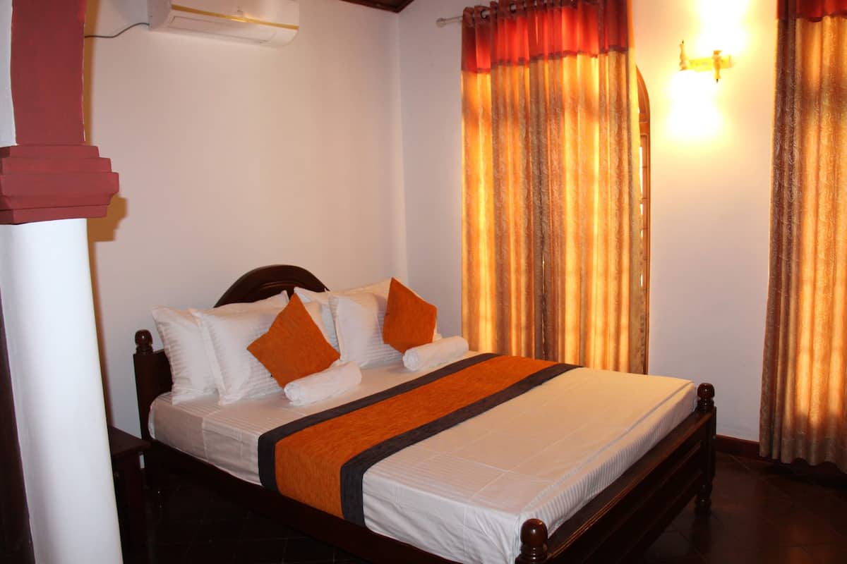 A neatly made bed with white and orange bedding, a wooden headboard, and a red pillar.