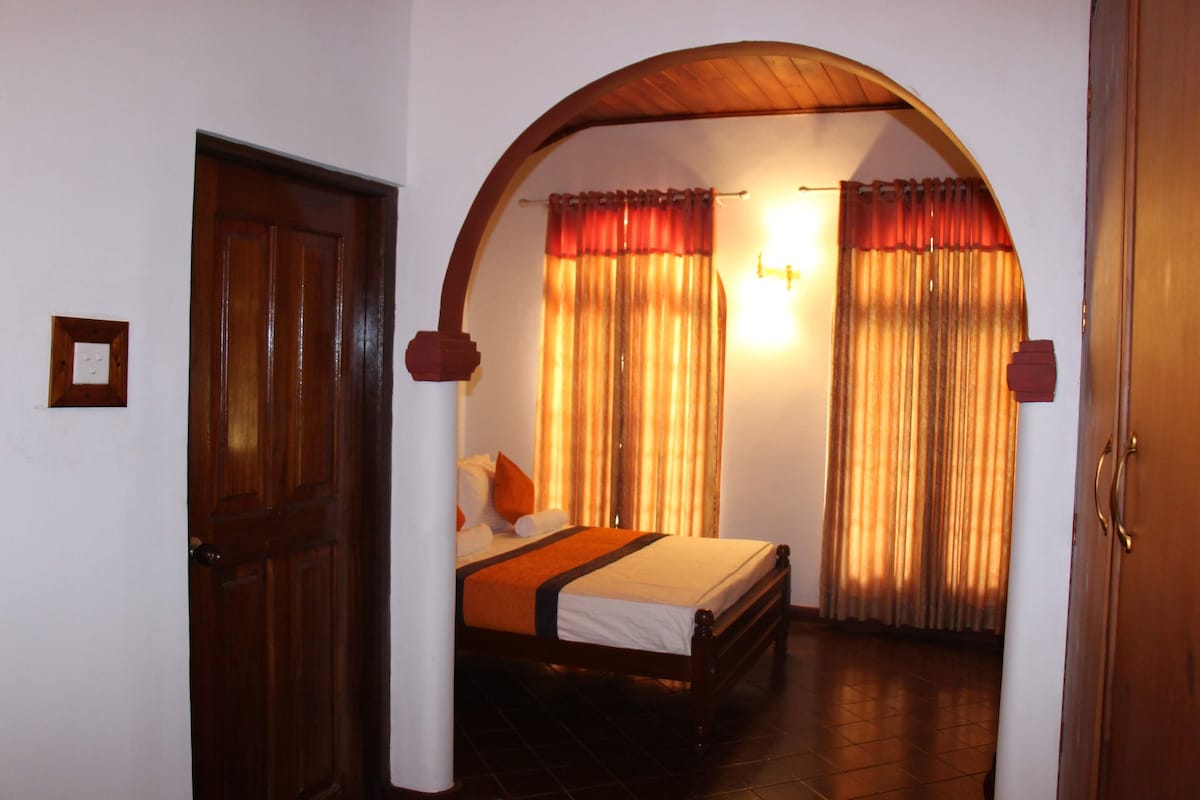 Una habitación con una cama, una puerta de madera y un aplique en la pared.