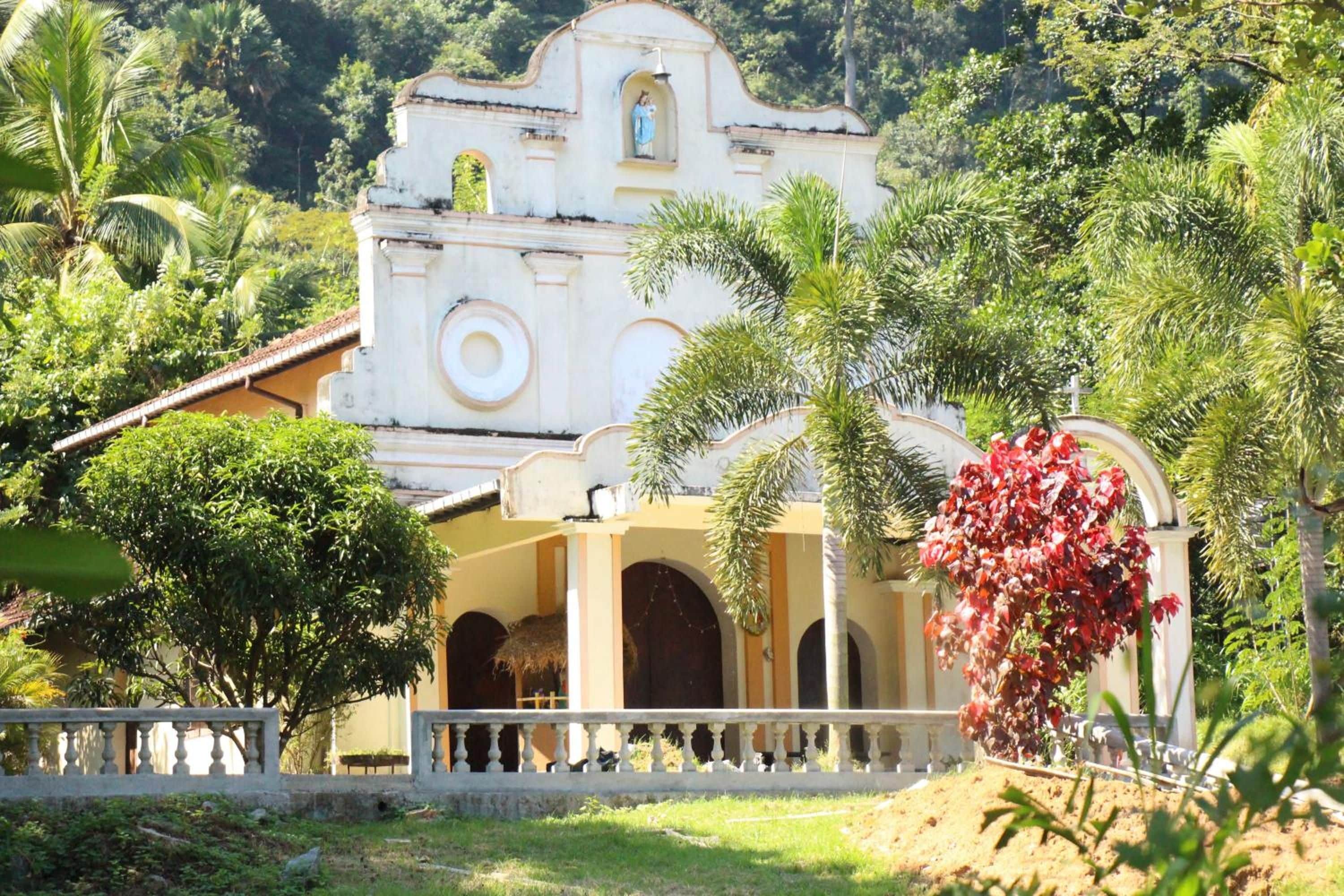 A colonial-style building with a central dome, surrounded by lush greenery and a decorative archway.