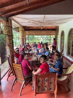 A group of people seated around a table in a covered outdoor area with wooden furniture and a bamboo structure overhead. - Xotic Resort (Mawathagama)