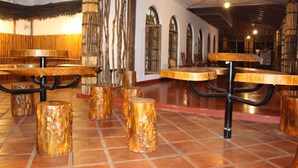 A restaurant interior with wooden tables and stools, bamboo columns, and tiled flooring.