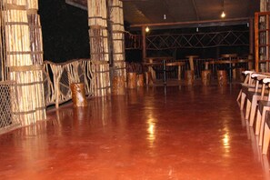 A spacious indoor area with a polished floor, wooden furniture, and a thatched wall structure. - Xotic Resort (Mawathagama)