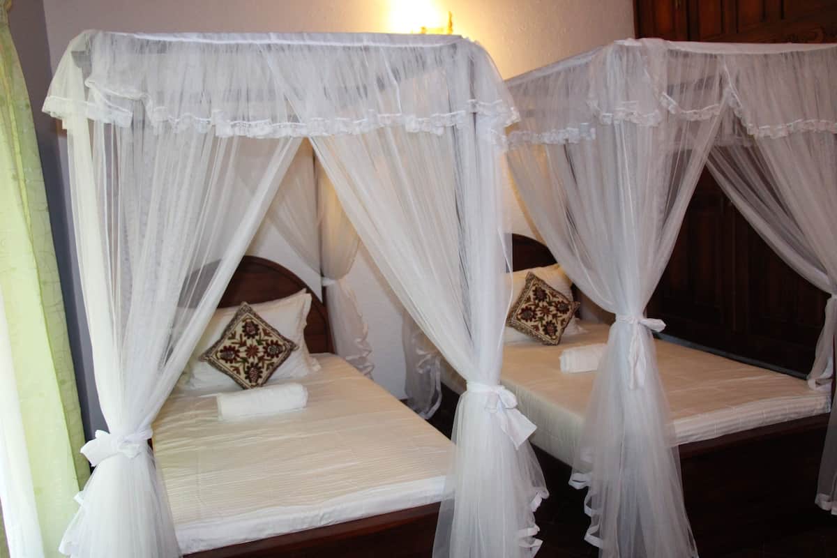 Two single beds with white bedsheets and decorative pillows, each with a canopy bedspread.