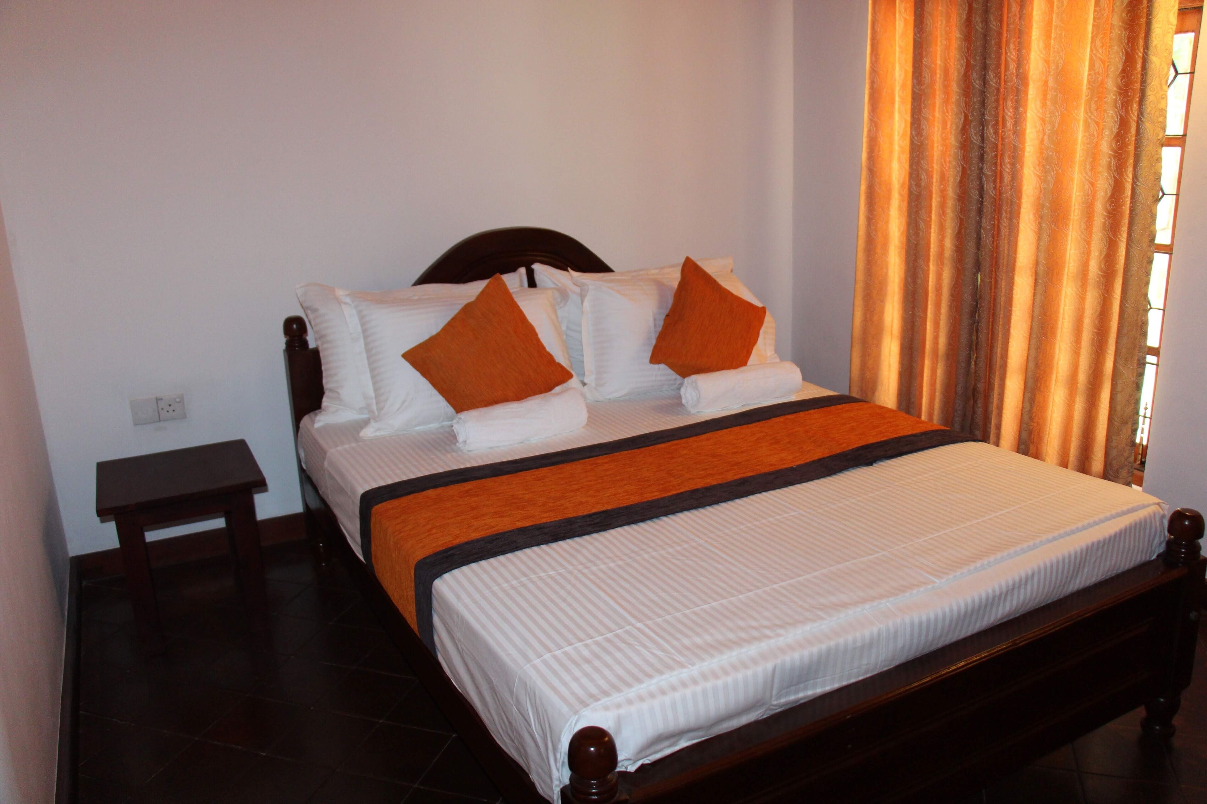 A neatly made bed with white linens and orange pillows, a wooden headboard, and a small bedside table.