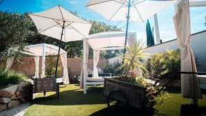 Ein Garten mit einer Terrasse, weißen Sonnenschirmen, einer Pergola und einem hölzernen Wagen mit Pflanzen.