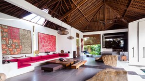 A spacious living area with a red sofa, wooden coffee table, and a large abstract painting. - Rent a Luxury Villa in Bali Close to the Beach, Bali Villa 2035 (Bali)