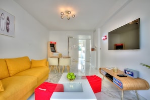 A modern living room with a yellow sofa, a white coffee table with a laptop and green apples, a wooden side table with a red box, and a large mirror on the wall.