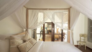 A bedroom with a canopy bed, a wooden chair, and a view of the dining area.