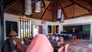 A spacious living area with a thatched roof, wicker furniture, and a dining area with a kitchen in the background. - How to Rent Your Own Private Luxury Holiday Villa in Seminyak for Less than Basic Hotel (Bali)