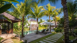 A tropical resort with a swimming pool, wooden deck, lounge chairs, and palm trees. - How to Rent Your Own Private Luxury Holiday Villa in Seminyak for Less than Basic Hotel (Bali)