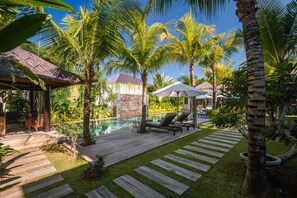 Ein tropisches Resort mit Schwimmbad, Holzterrasse, Liegestühlen und Palmen.