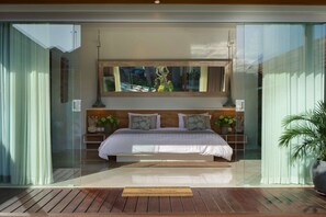 A modern bedroom with a large bed, a wooden headboard, and a view of a garden through a glass door. - Imagine Your Family Renting a Luxury Holiday Villa Close to Seminyak’s Main Attractions (Bali)