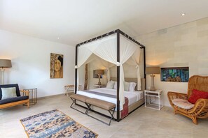Un dormitorio amplio con una cama con dosel, un banco, una silla de ratán y una alfombra estampada.