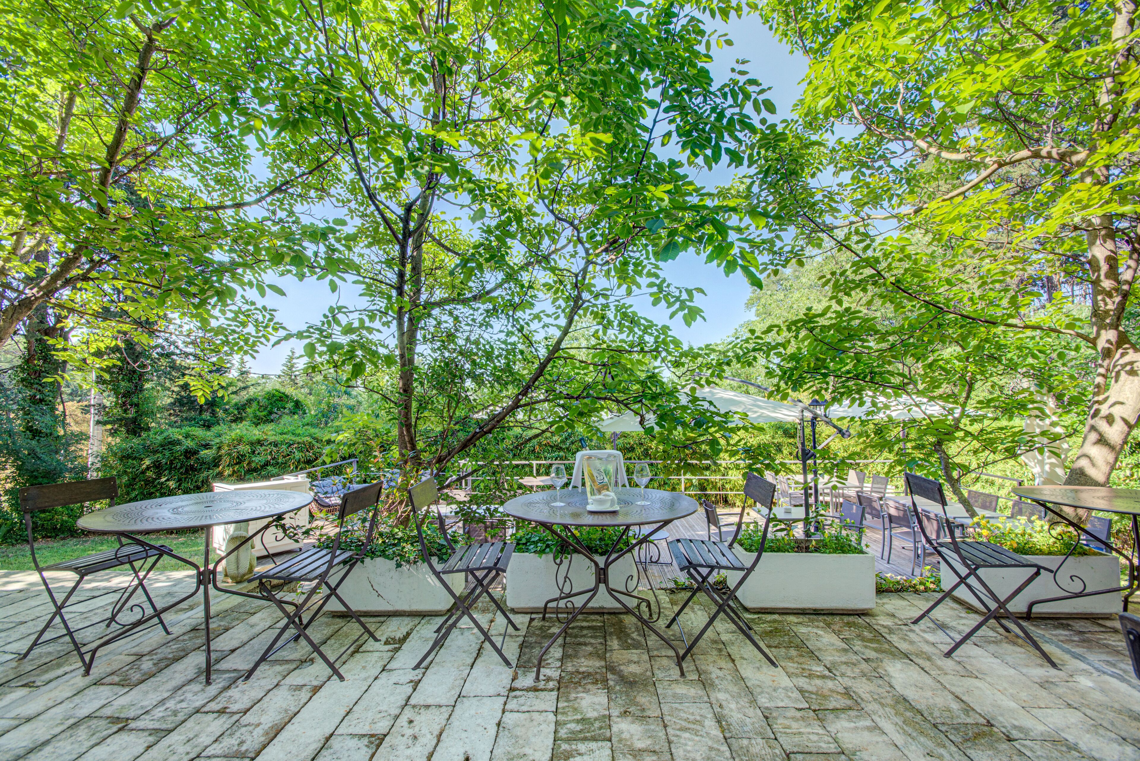 Une terrasse extérieure avec une table ronde et des chaises, entourée de verdure et d’arbres.