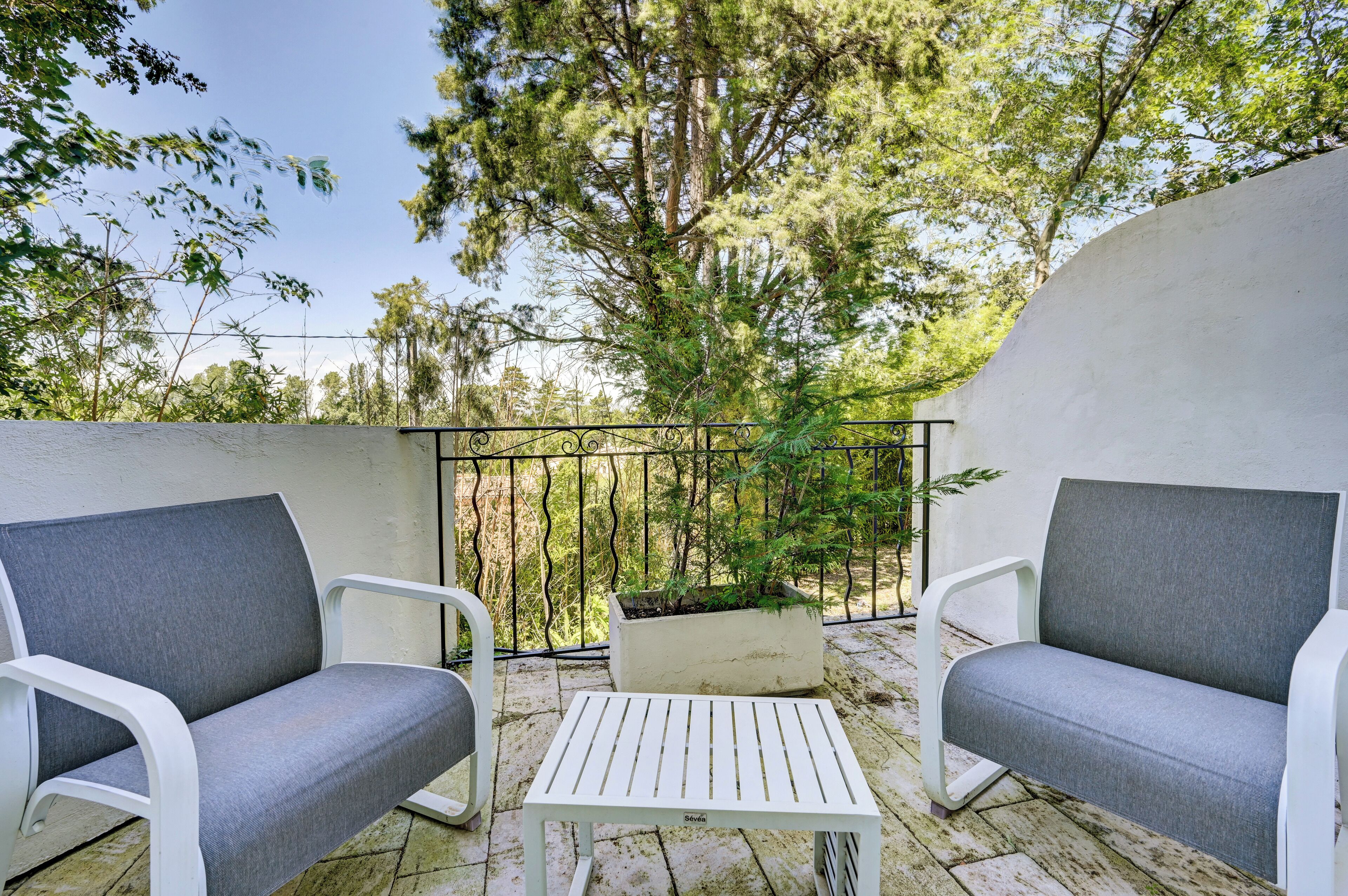 A balcony with two grey upholstered chairs, a white table, and a potted plant.