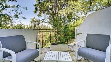 A balcony with two grey upholstered chairs, a white table, and a potted plant.