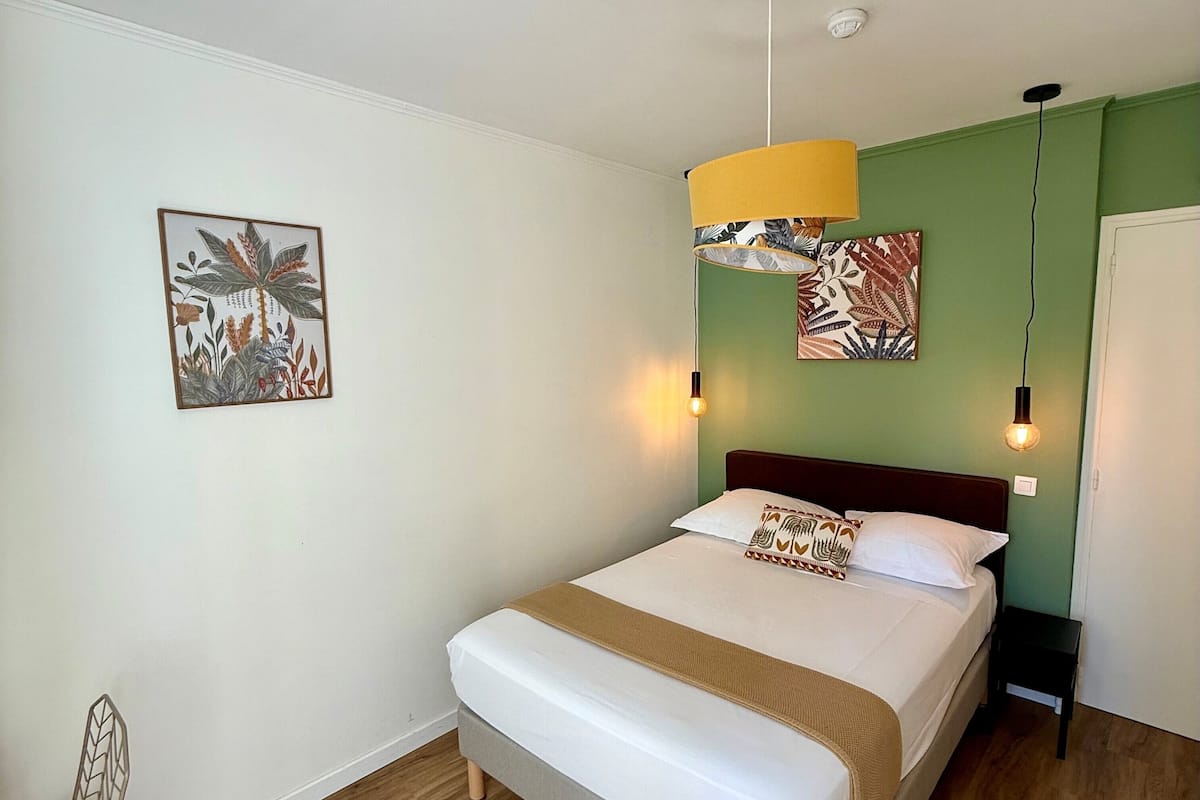 A neatly made bed with a brown throw blanket, a headboard, and a wall-mounted light fixture.