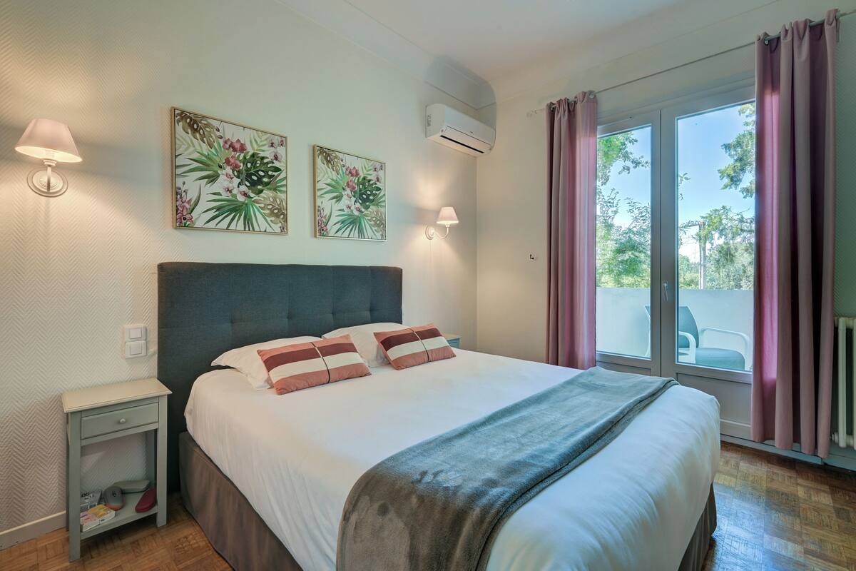 A bedroom with a bed, two wall-mounted lamps, a nightstand, and a window with curtains.