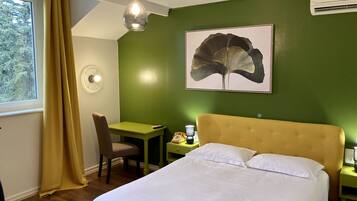 Habitación de hotel con cama, escritorio, silla, lámpara y una obra de arte con forma de hoja grande en la pared.