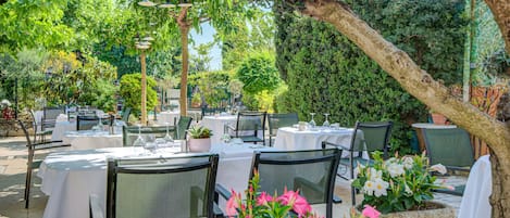 An outdoor dining area with tables and chairs, surrounded by greenery and trees.