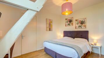 A bedroom with a bed, a nightstand, a wall-mounted lamp, and two framed pictures.