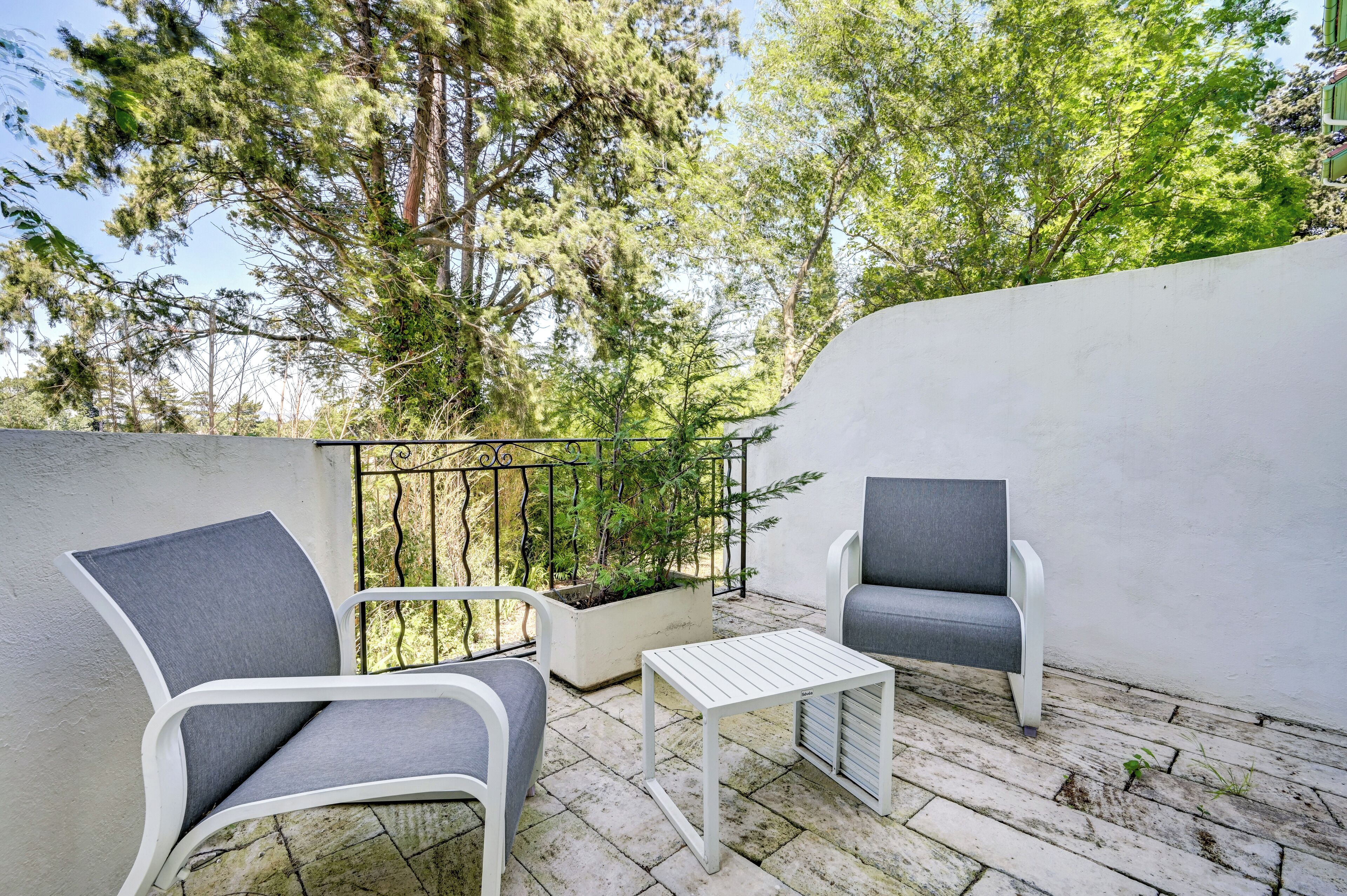 A balcony with two grey chairs, a small white table, and a potted plant.