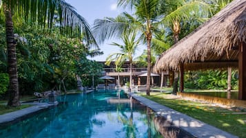 Una piscina rodeada de palmeras y una estructura con techo de paja.