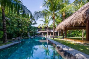 A pool surrounded by palm trees and a thatched-roof structure.