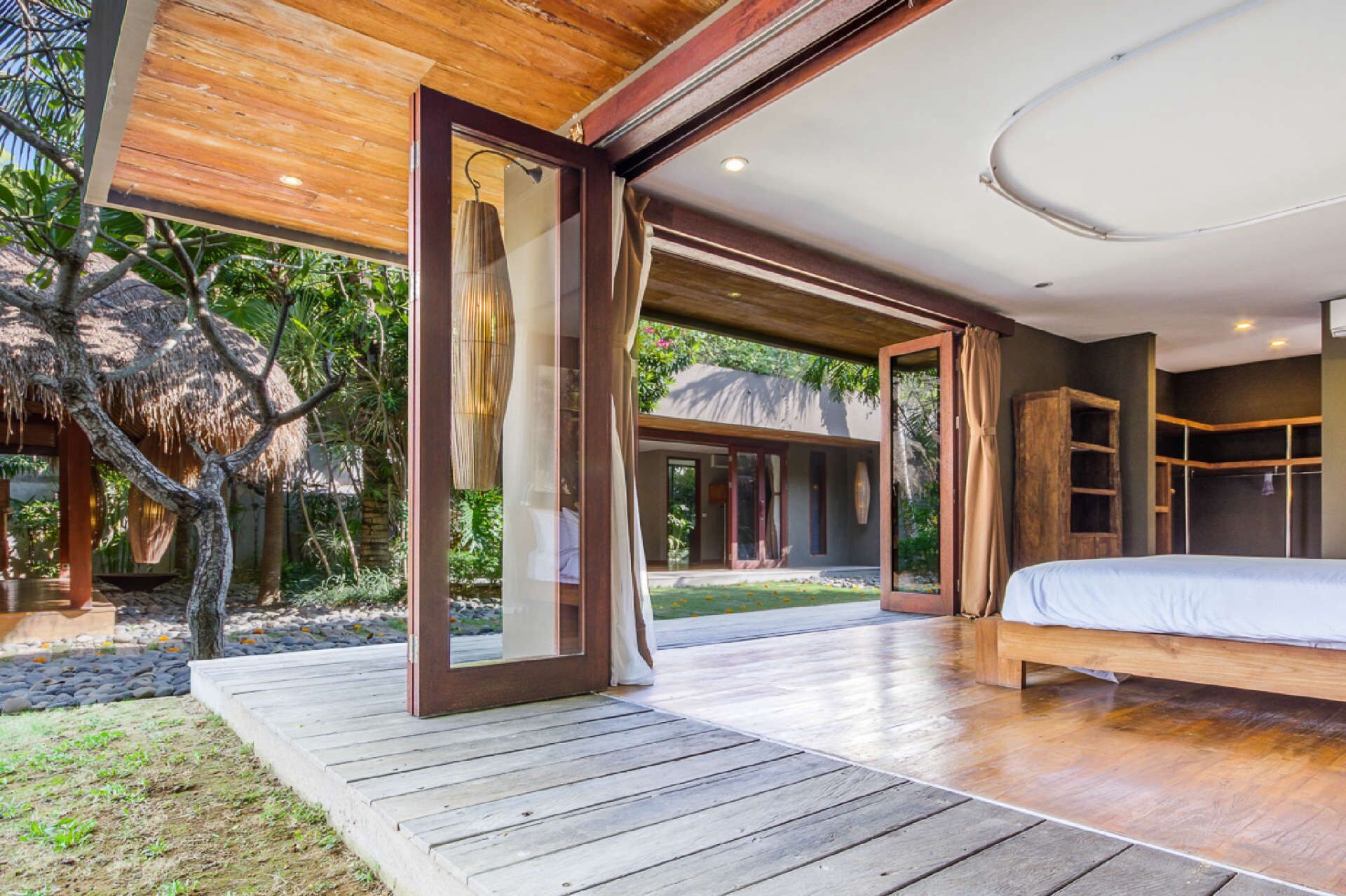 Un dormitorio moderno con una cama grande, suelo de madera y vistas a un jardín tropical.