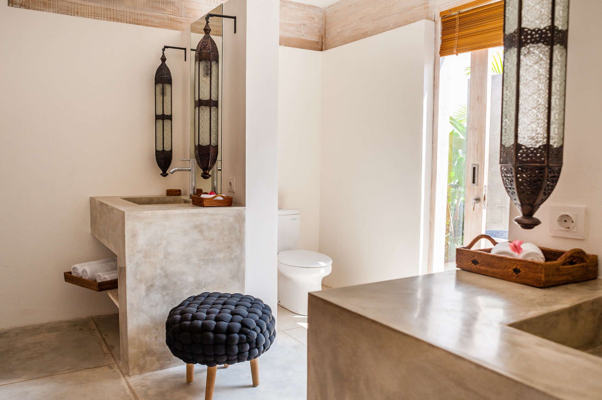 A modern bathroom with a concrete sink, a white toilet, and a black ottoman.