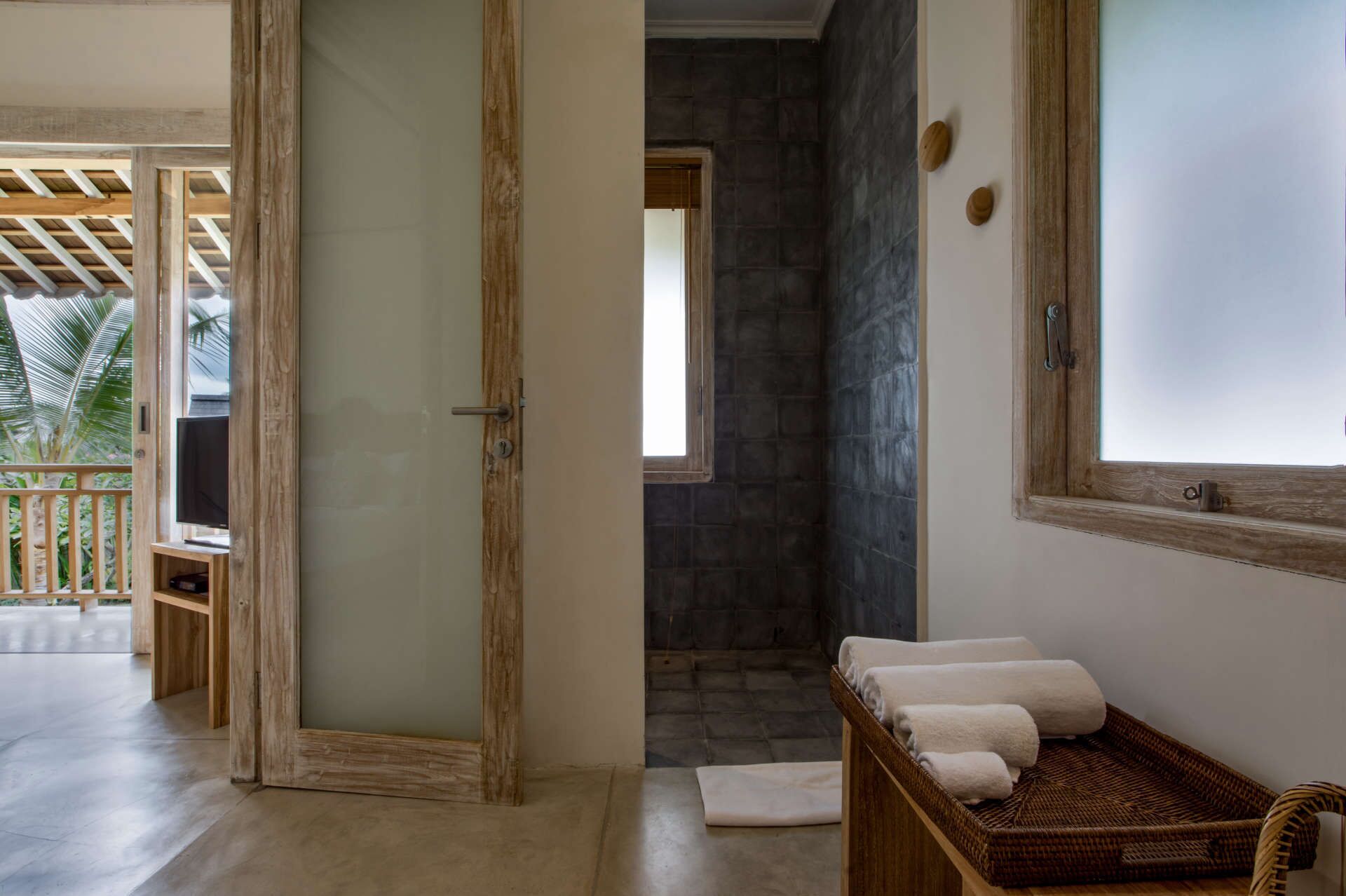 Un baño con pared de piedra, puerta de madera y una cesta de mimbre con toallas.