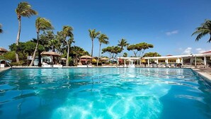 Una piscina azul cristalina rodeada de palmeras y sillas de descanso, con un edificio al fondo.