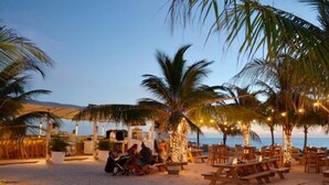 Un restaurante frente al mar con terraza, palmeras y luces colgantes.