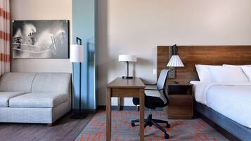 Une chambre d’hôtel avec un lit, un bureau, une chaise, un canapé et une lampe.