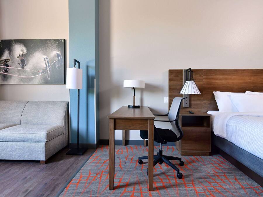 Une chambre d’hôtel avec un lit, un bureau, une chaise, un canapé et une lampe.